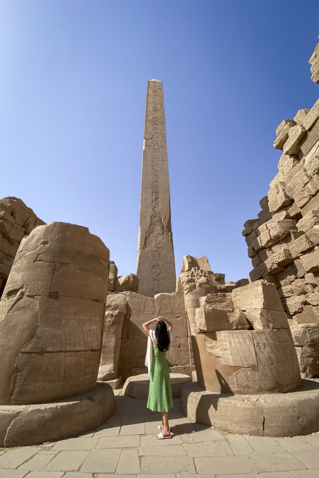 Top Ancient Sights in Egypt: Travel Blogger Jordan Gassner wearing a green dress and shielding her eyes while looking up at Hatshepsut's Obelisk in Karnak Temple