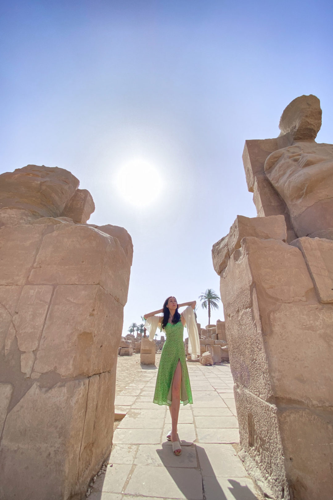 Top Ancient Sights in Egypt: Travel Blogger Jordan Gassner wearing a green dress looking up at a statue with hands behind head and a cream scarf while walking between the a former passage at Karnak Temple