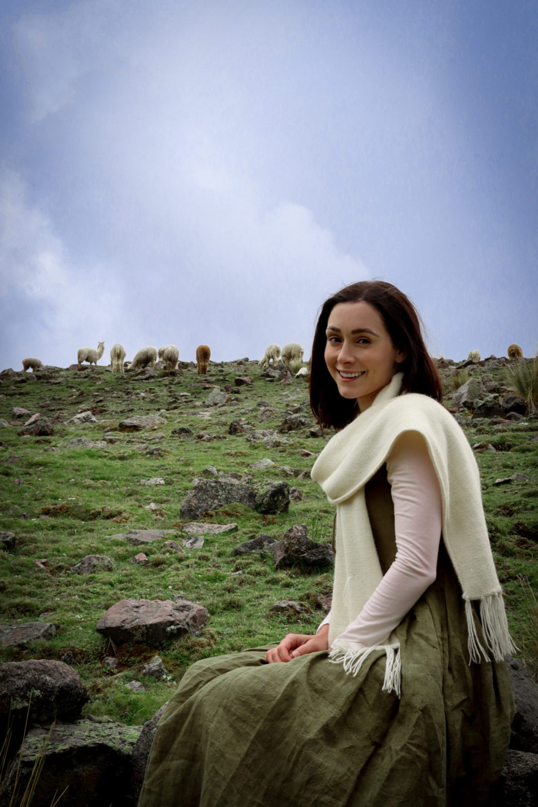 Travel Blogger Jordan Gassner smiling at camera and sitting on a rock while surrounded by wild alpacas on the Ausangate 7 Lakes Trek near Cusco, Peru