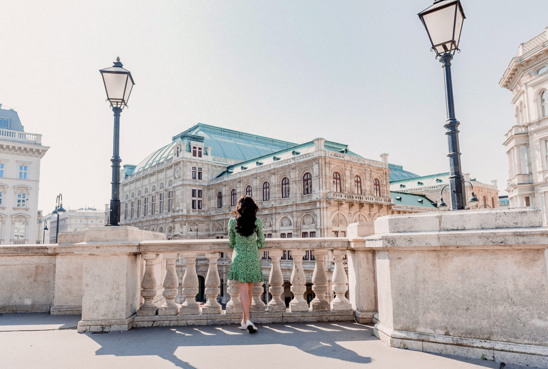 Vienna Travel Guide: Travel Blogger Jordan Gassner wears a green mini dress and peers off a balcony at the Vienna State Opera House