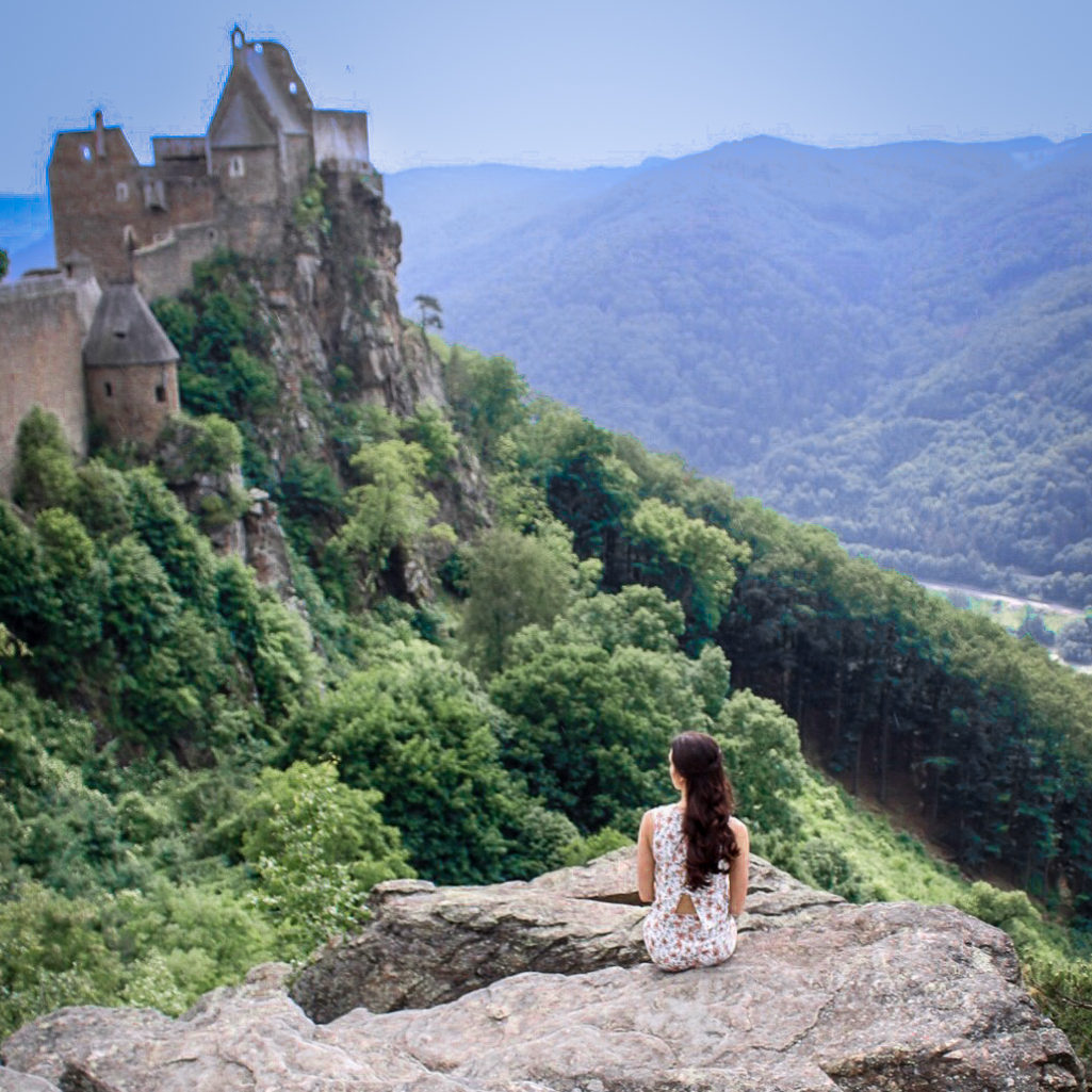 Travel Blogger Jordan Gassner sitting cliffside in front of Aggstein Castle in the Wachau Valley on a day trip from Vienna