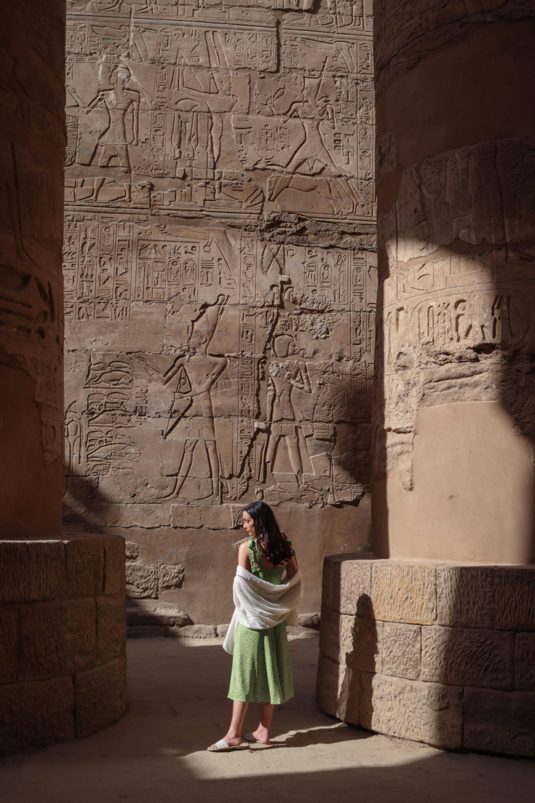 Travel Blogger Jordan Gassner wearing a green dress and standing just outside the shadows from the columns in Karnak Temple's Hypostyle Hall in Luxor, Egypt
