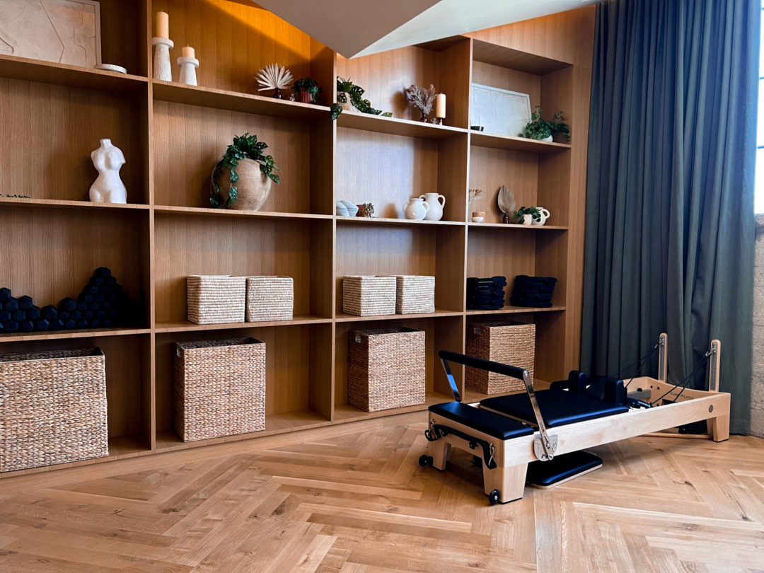 A pilates machine in front of a bookshelf with plants, candles, art pieces and workout equipment in the Pilates Studio of Heimat Club