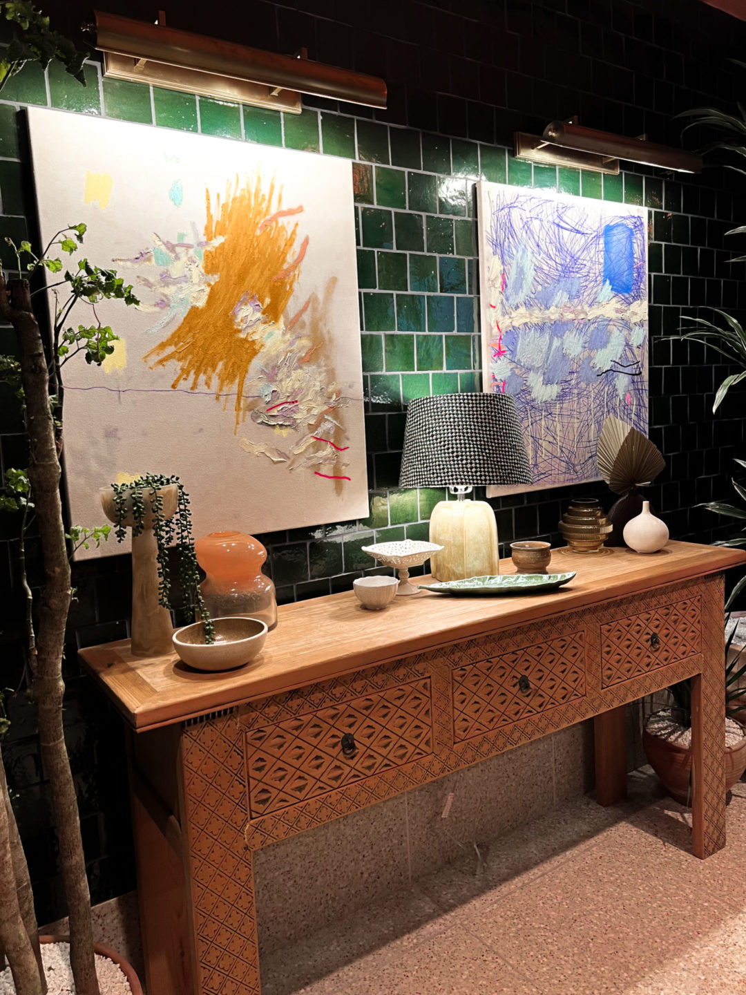 Two vibrantly abstract paintings above a sidetable with beautiful plants, pots and lights inside a hallway of Heimat in Los Angeles