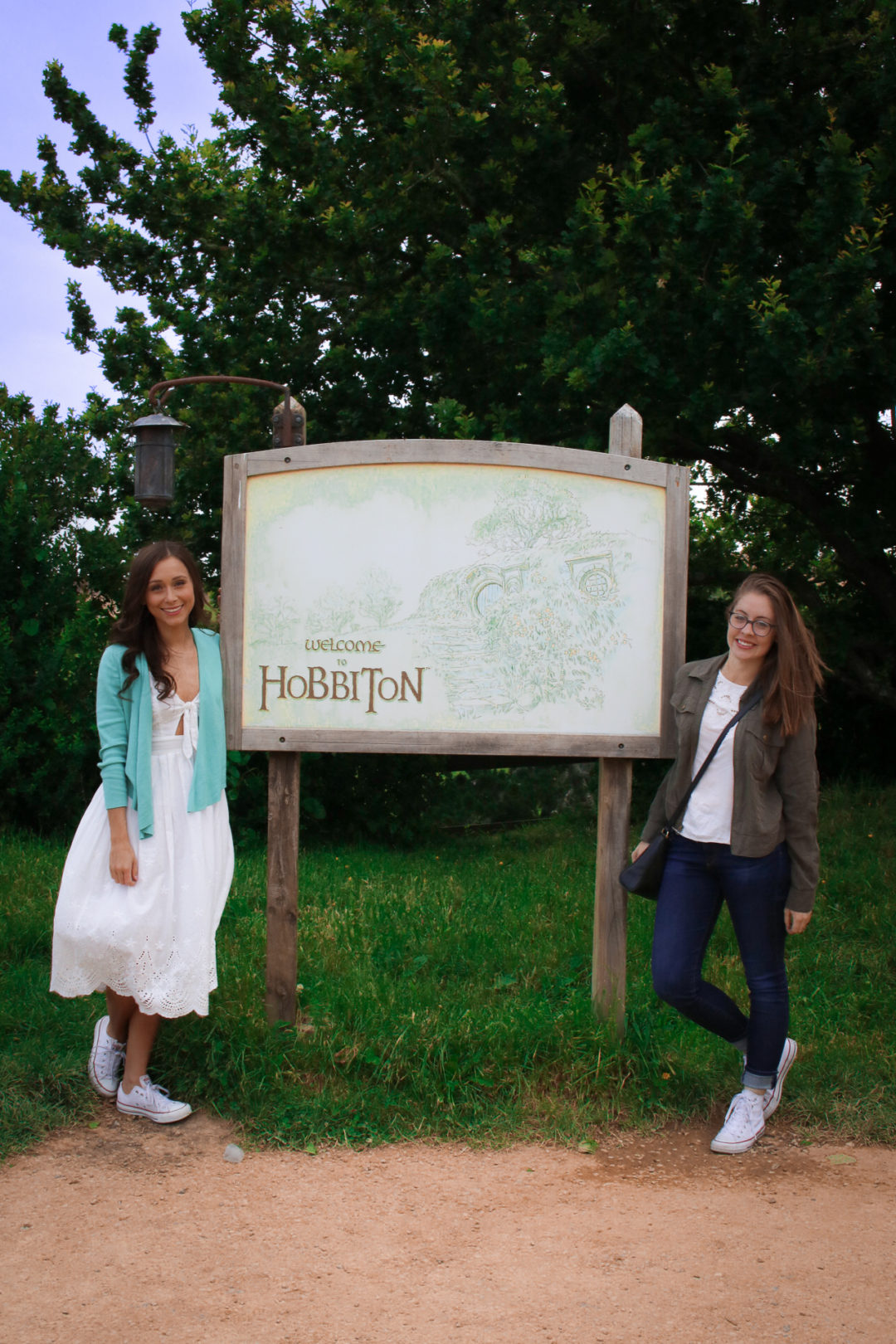 Travel Blogger Jordan Gassner and friend standing in front of a "Welcome to Hobbiton" sign and map in Hobbiton New Zealand