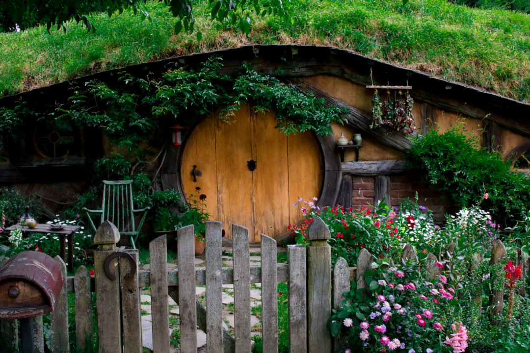 A yellow door and colorful flower garden behind a short closed gate in Hobbiton New Zealand