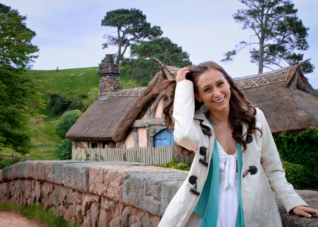 Travel Blogger Jordan Gassner smiling in front of the Mill in Hobbiton New Zealand