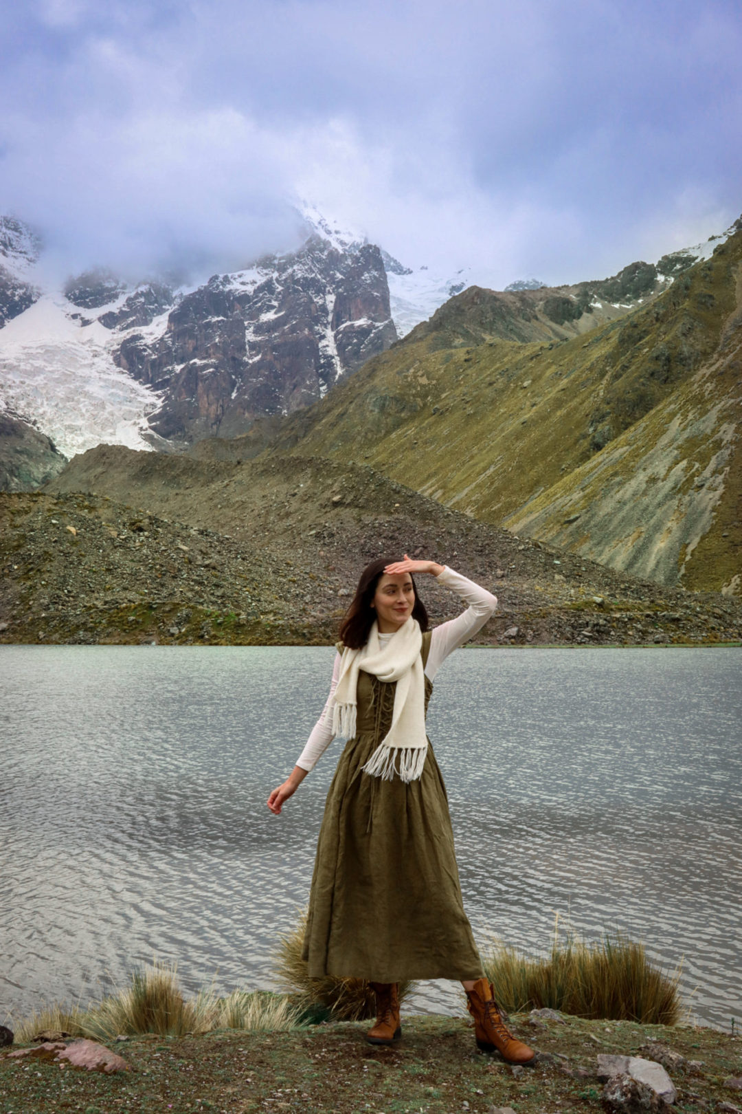 Jordan Gassner shielding her eyes while wearing a vintage Sound of Music inspired dress in front of a lake on the Ausangate Trail