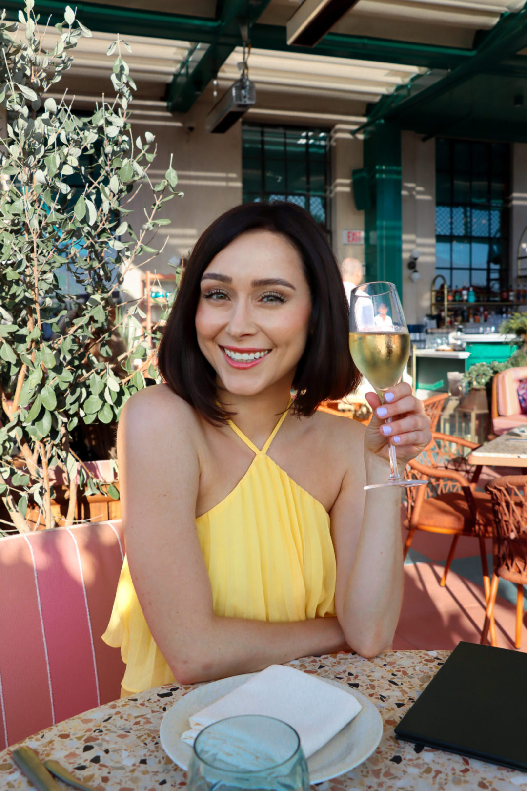 Travel Blogger Jordan Gassner holding champagne and dining outside at Mother Tongue Restaurant in Los Angeles