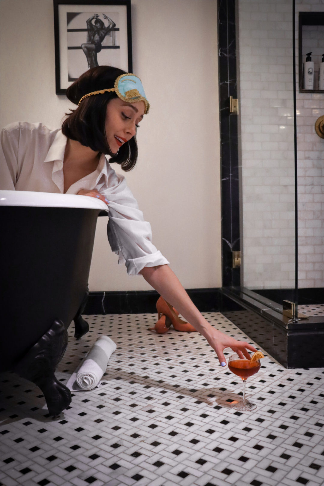 Travel Blogger Jordan Gassner wearing a Breakfast at Tiffany's-inspired outfit and reaching for a cocktail in a clawfoot tub at the Prospect Hollywood Hotel