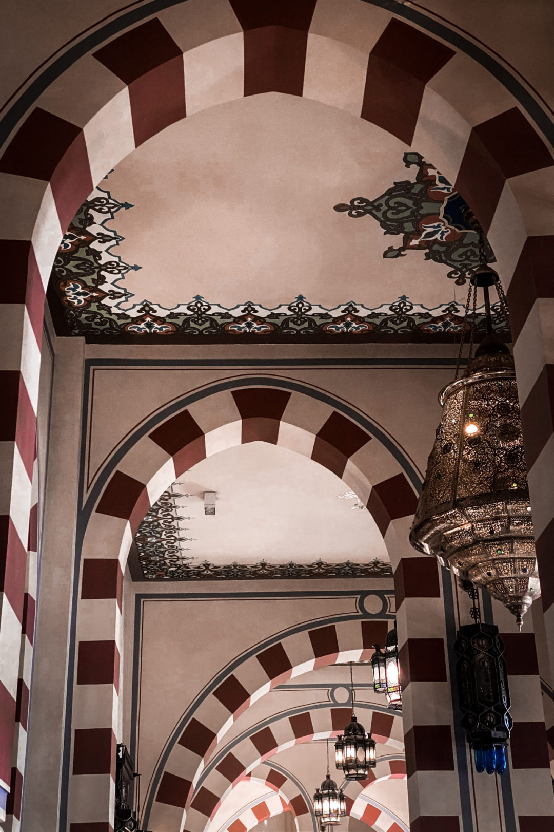 A blue and gold patterned ceiling peeking out between red and cream striped columns inside the Sofitel Legend Old Cataract Hotel