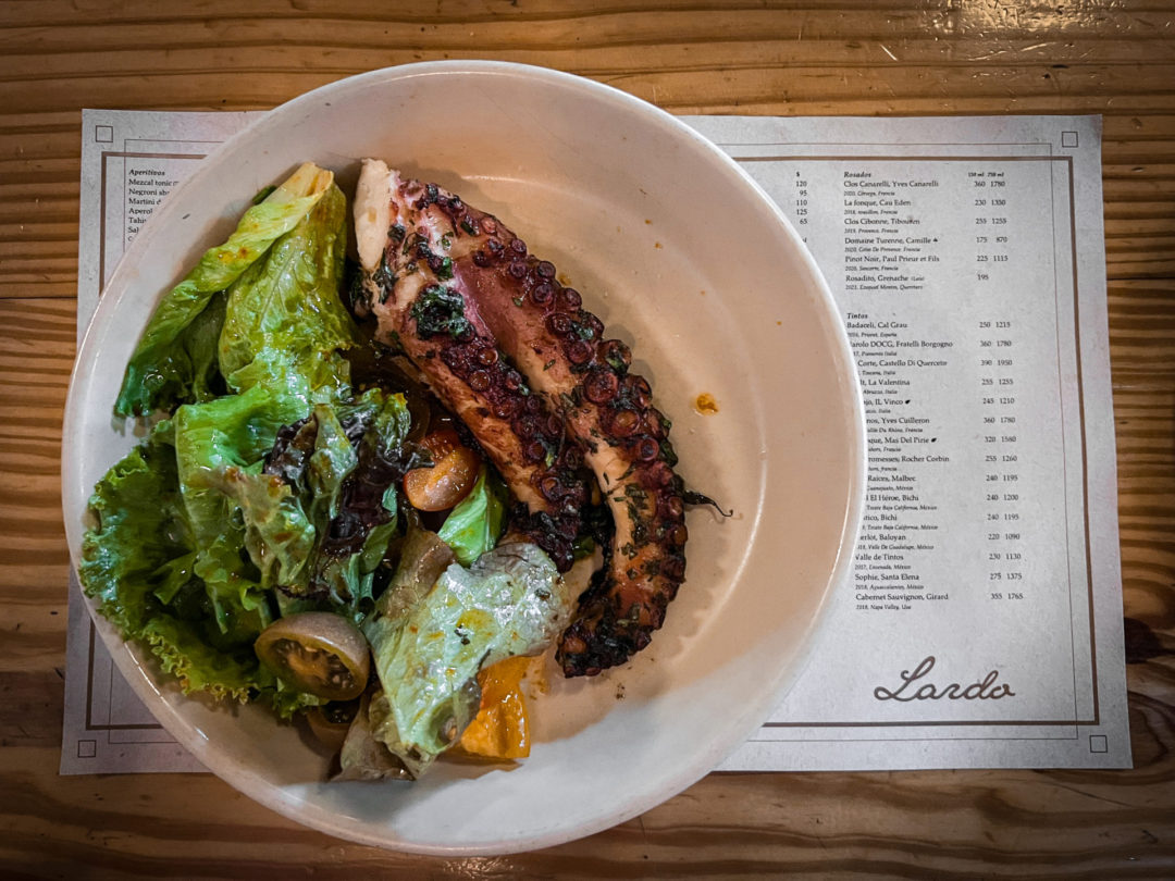 A plate with fried octopus and a side salad sit on top of a Lardo Restaurant menu in CDMX
