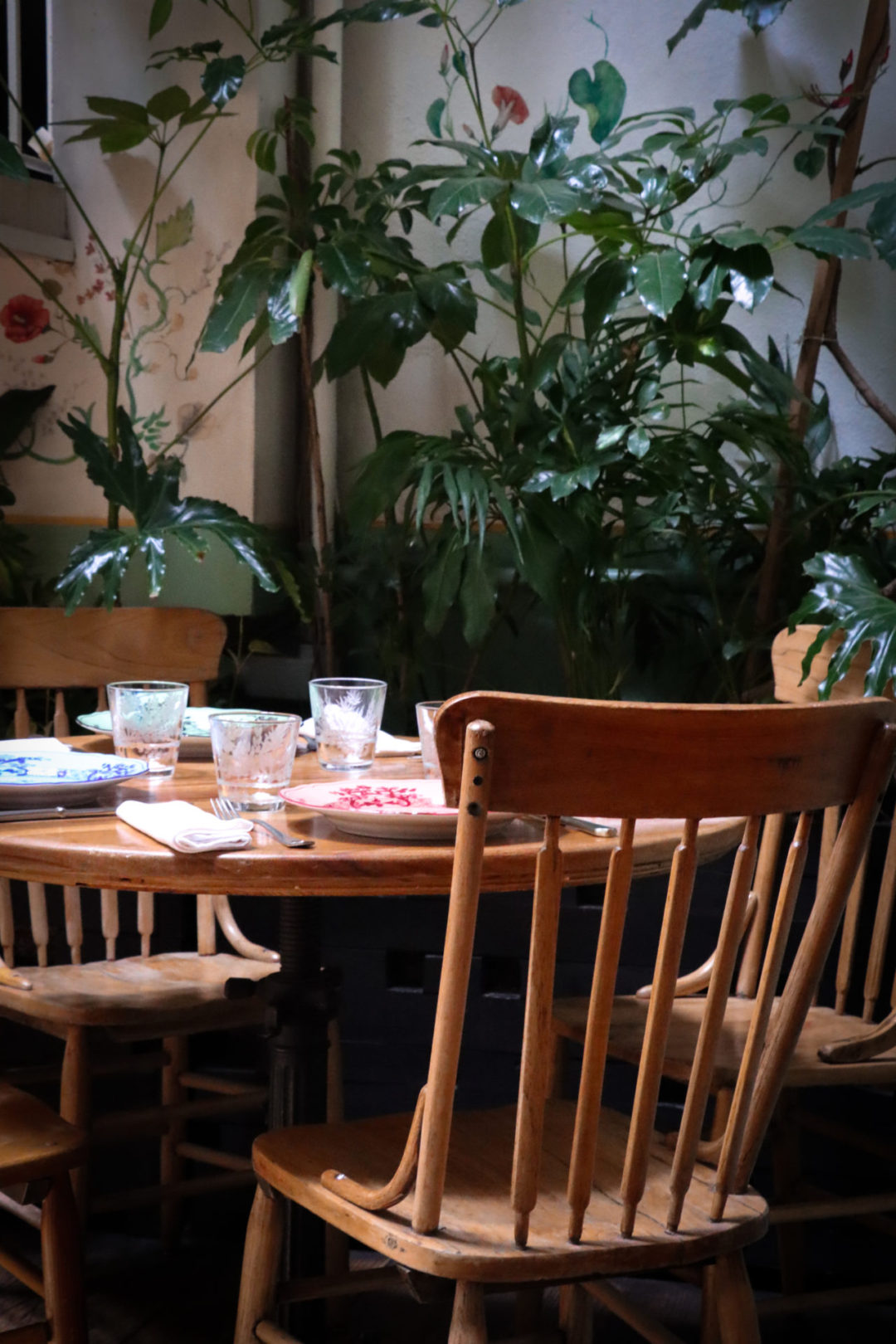 An empty wooden table and chairs with colorful china surrounded by green plants inside Restaurante Rosetta in Mexico City