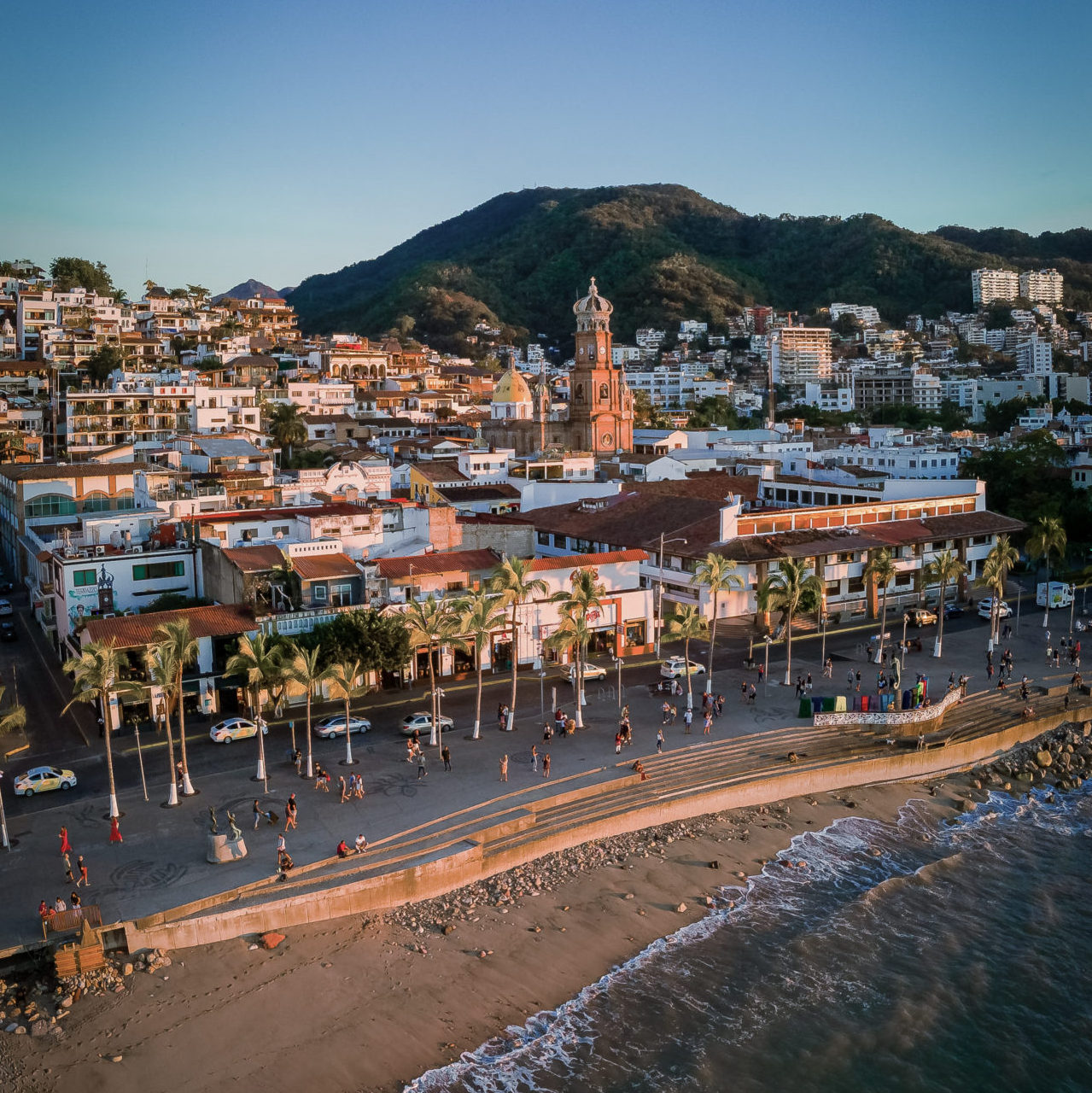 Aerial view of the Puerto Vallarta beach and town at sunset, with the cathedral raising up in the background.