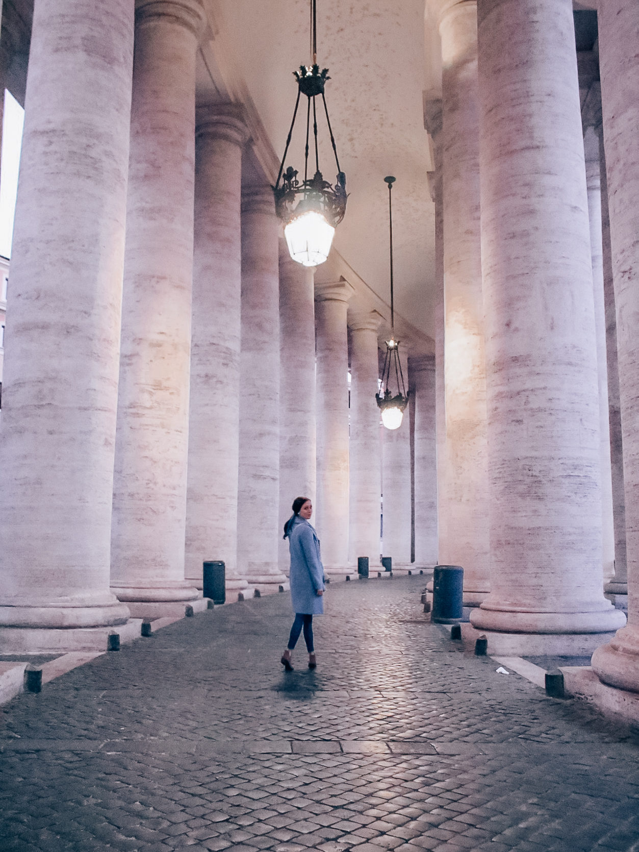 Travel Blogger Jordan Gassner smiling to a tripod camera setup while standing in one of Vatican City's colonnades