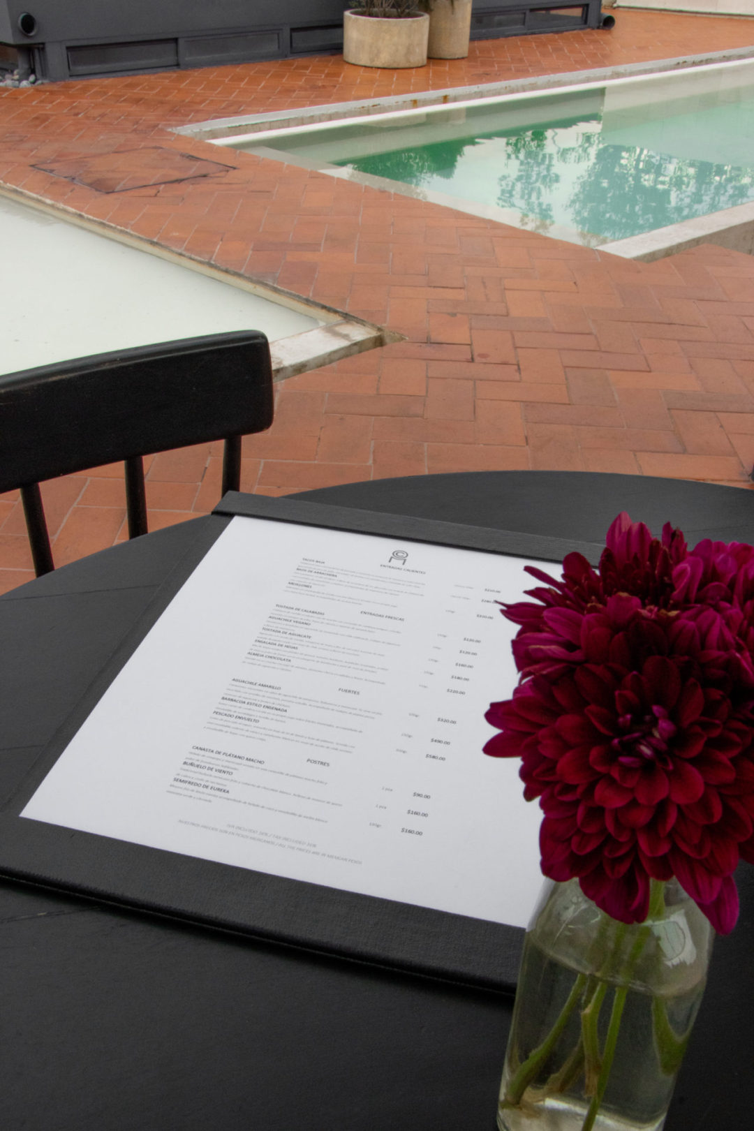 A food menu and purple flowers sit on a black table near the rooftop pool at Círculo Mexicano in El Centro, CDMX, Mexico