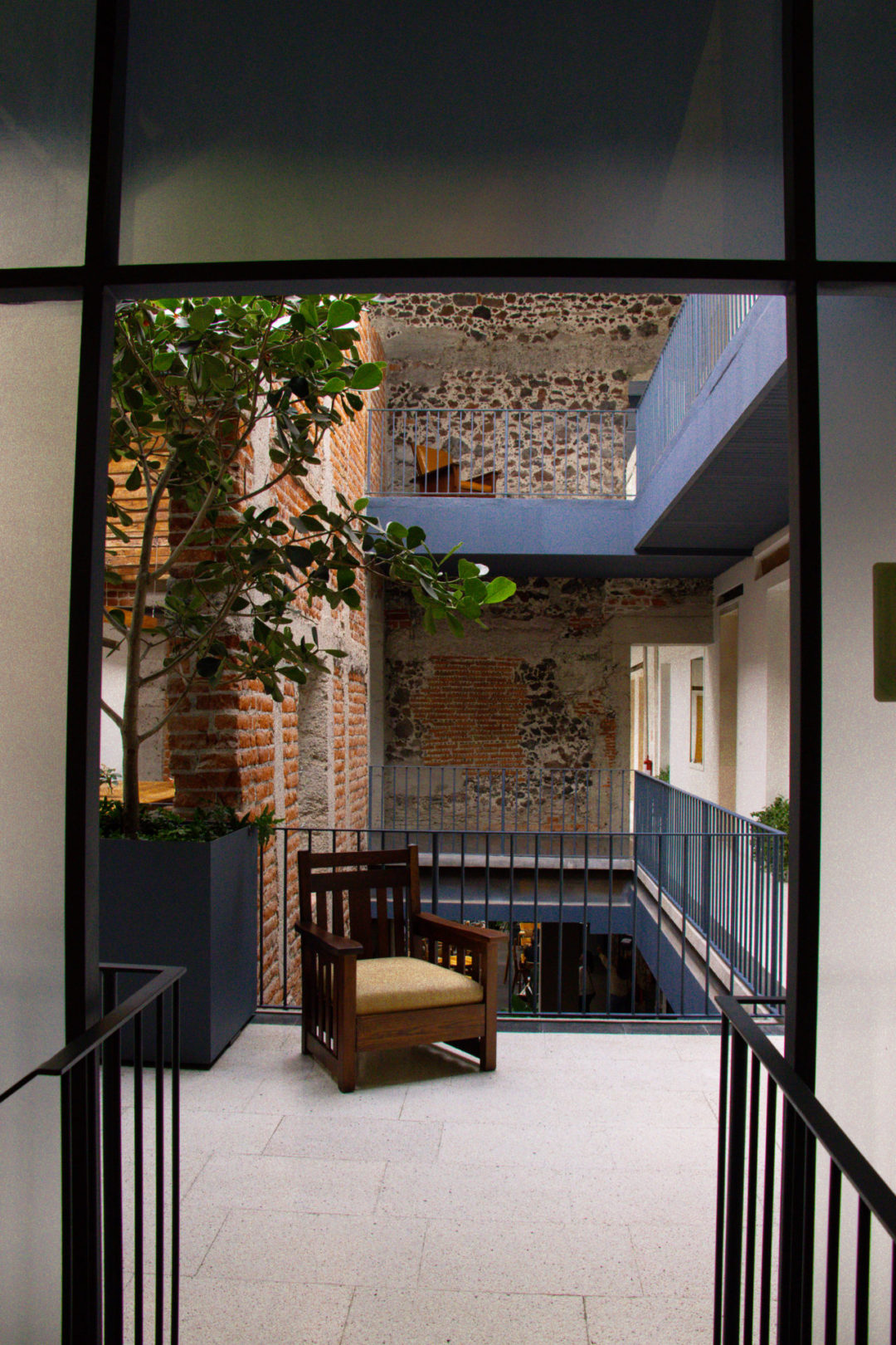 A wooden chair in front of a balcony and old brick wall inside the Círculo Mexicano boutique hotel in Mexico City