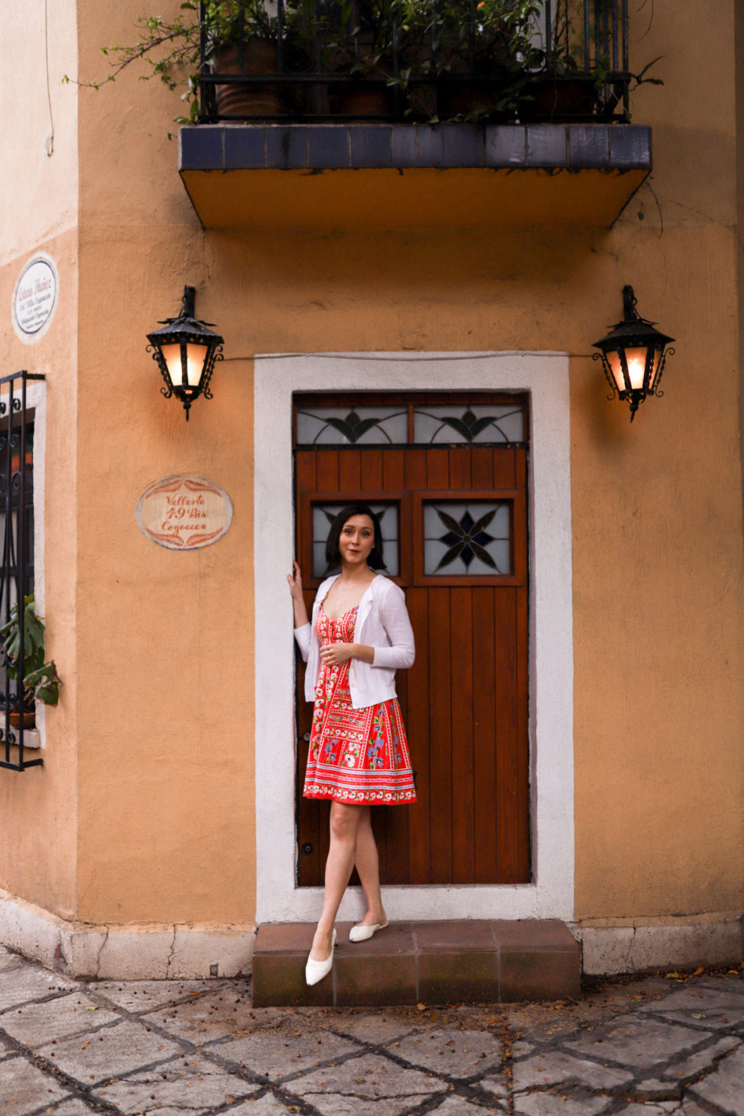 Travel Blogger Jordan Gassner stepping out from a wooden doorway of a light orange painted home in Coyoacán Mexico City
