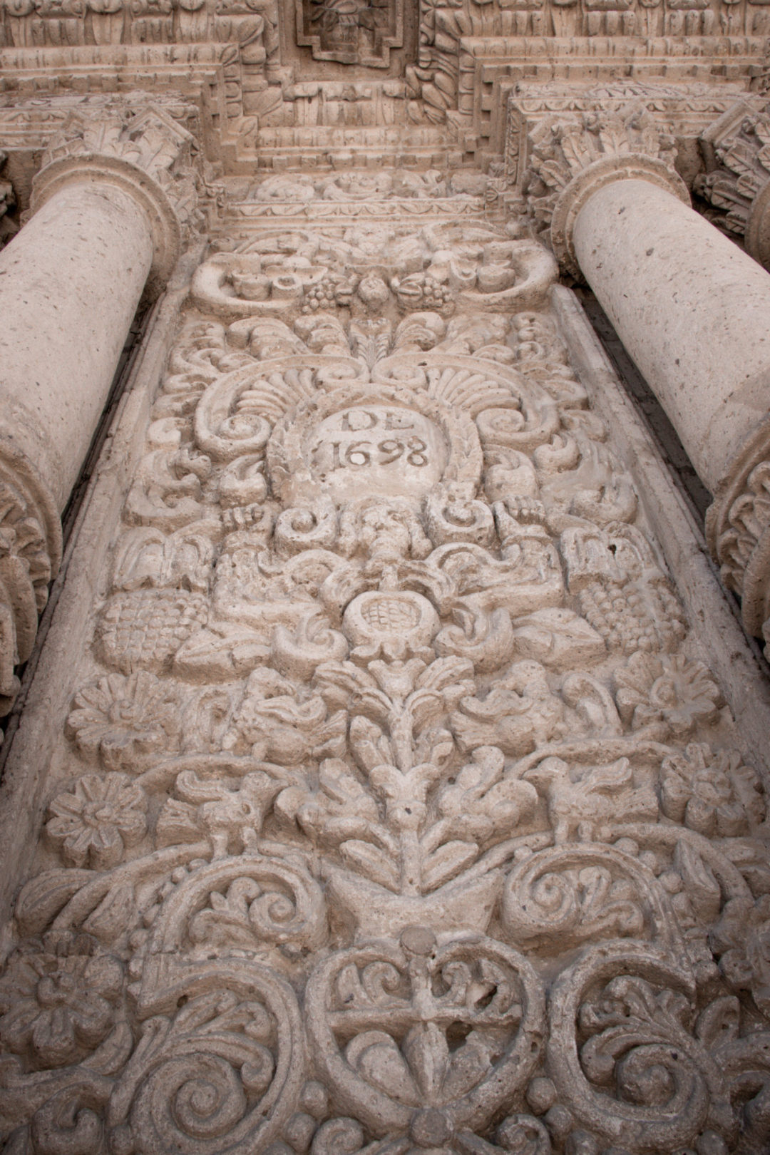 Intricate sillar-based carvings of flowers and plants surrounding a shield with the words "DE 1698") at Iglesia de la Compañía in Arequipa