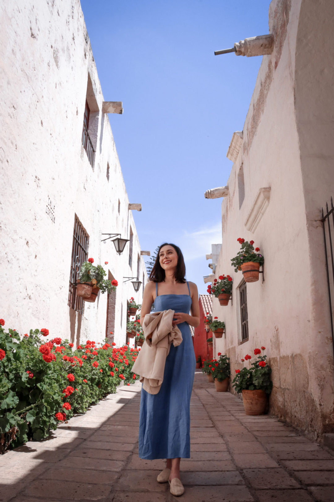 Travel Blogger Jordan Gassner walking down a row of red flowers inside of the best sights in Arequipa: Santa Catalina Monastery