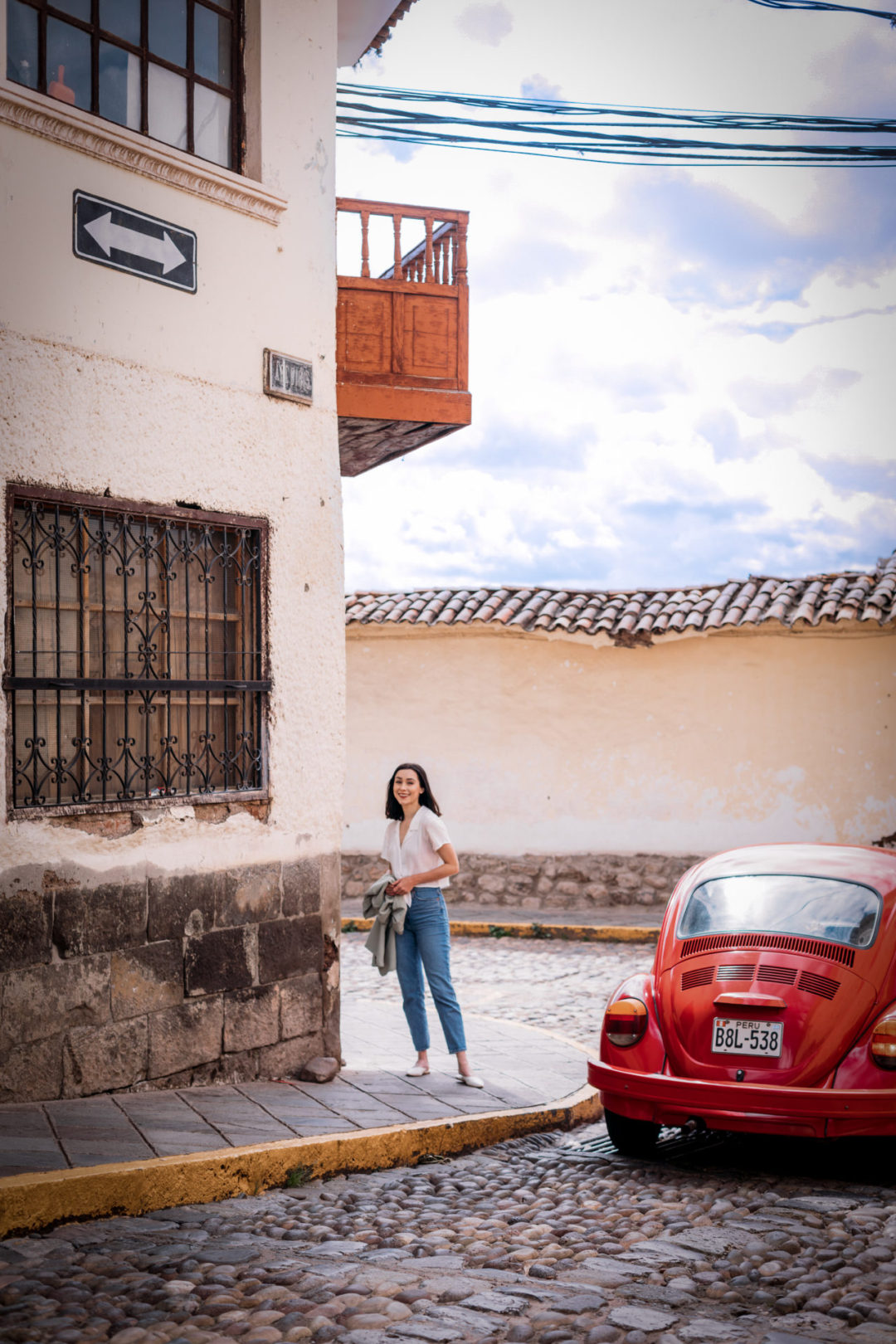 Travel Blogger Jordan Gassner standing and smiling near a corner while a red vintage bug passes by in Cusco, Peru