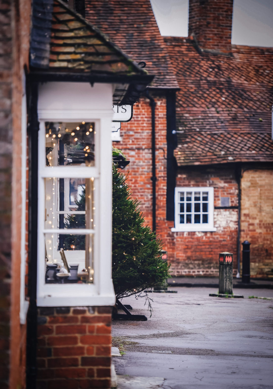 A classic red brick village with white windows decorated with strings of warm lights and a Christmas tree.