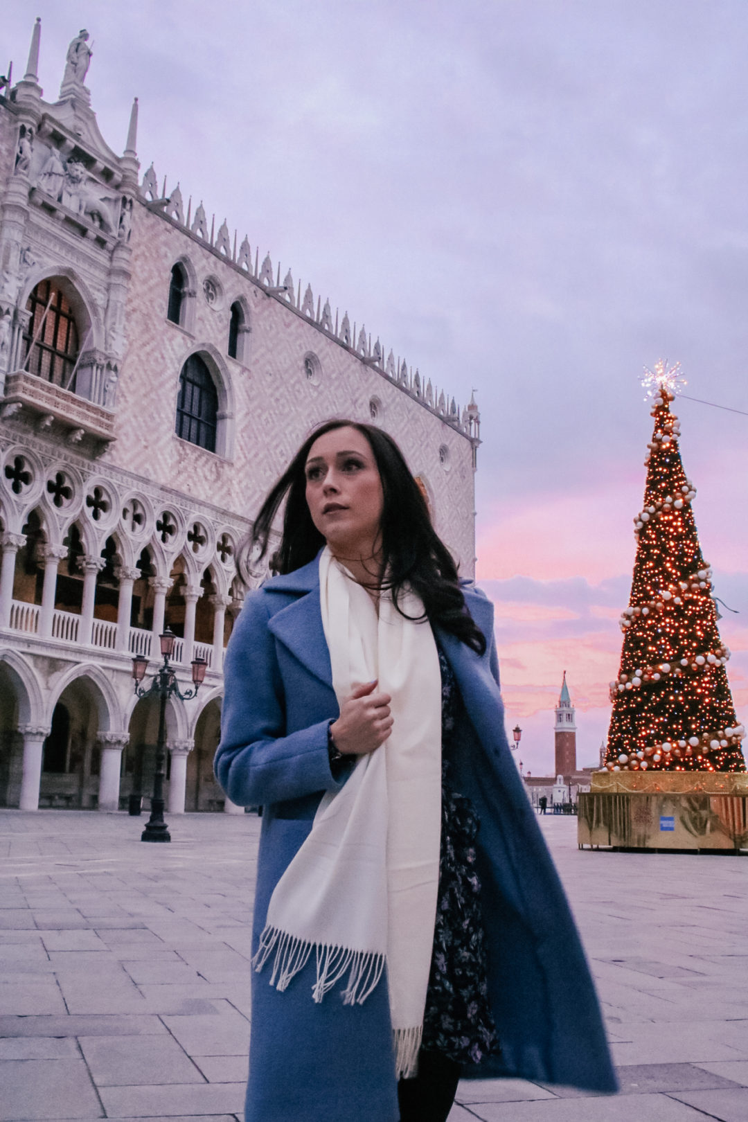 Travel Blogger Jordan Gassner walking by a Christmas Tree in front of Doge's Palace in Venice, Italy under a pink and purple sunrise