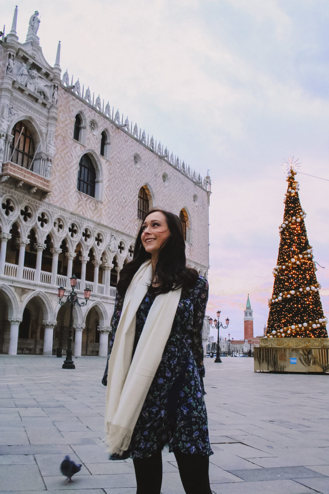 Travel Blogger Jordan Gassner smiling in front of a Christmas Tree in front of Doge's Palace in Venice, Italy under a purple sunrise