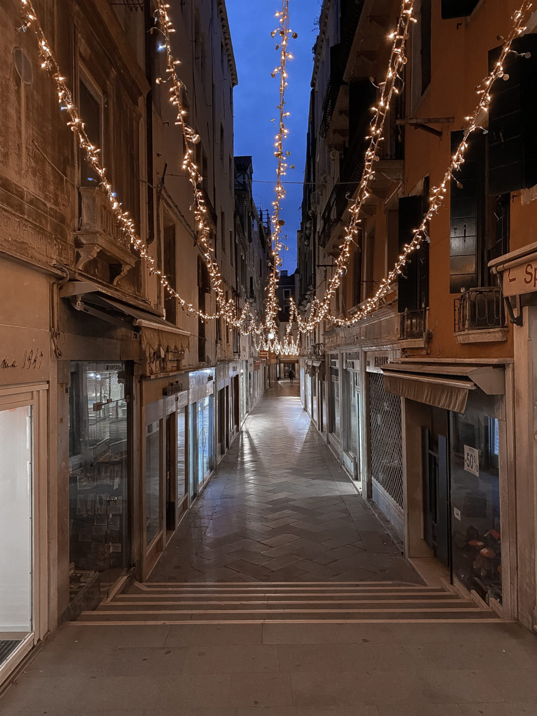 An alleyway of Christmas lights twinkling under a blue twilight sky in Venice, Italy