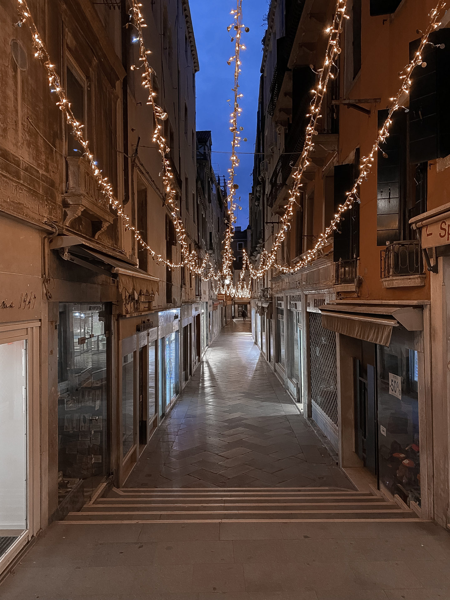 An alleyway of Christmas lights twinkling under a blue twilight sky in Venice, Italy