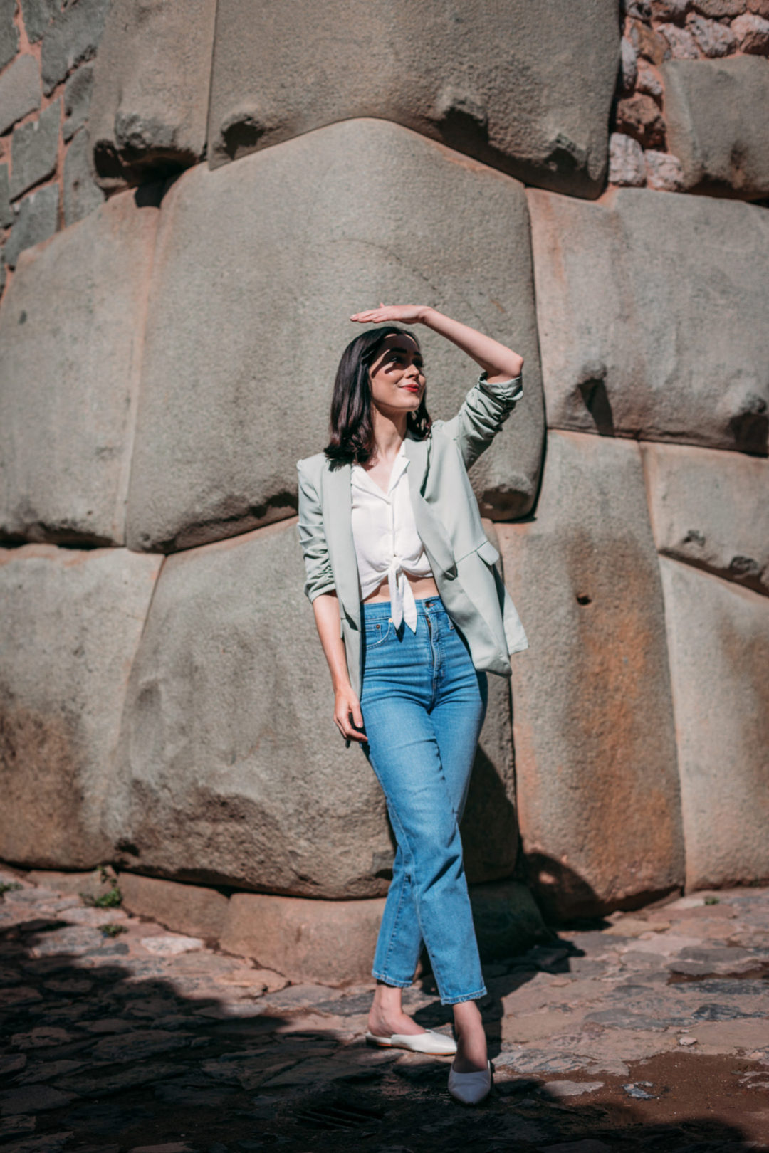 Travel Blogger Jordan Gassner shielding her eyes from the sun in front of the 12 Angled Stone in Cusco, Peru