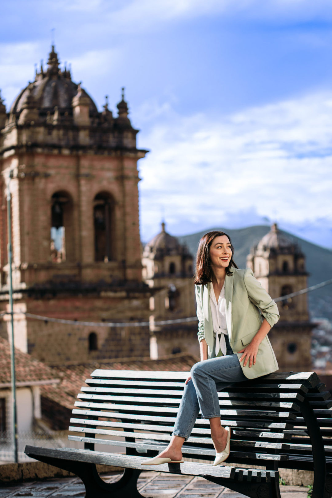 Travel Blogger Jordan Gassner leaning forward and smiling while sitting on a bench in Cusco, Peru's Plaza Tricentenario