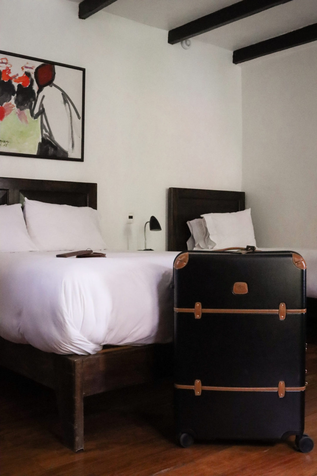 A Brics Milano Suitcase standing in front of one of two beds in a room at El Albergue Ollantaytambo in Peru