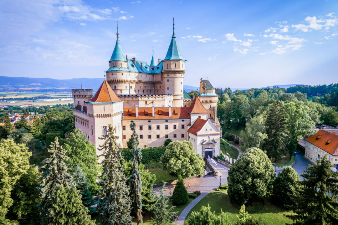 Bojnice Castle colorful facade sitting in the middle of a tree glen under a bright blue sky in Slovakia
