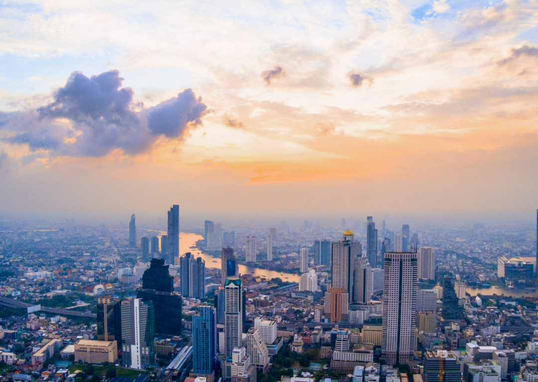 Last minute international travel destinations: An aerial view of the Bangkok skyline under an orange and purple sunset in Thailand