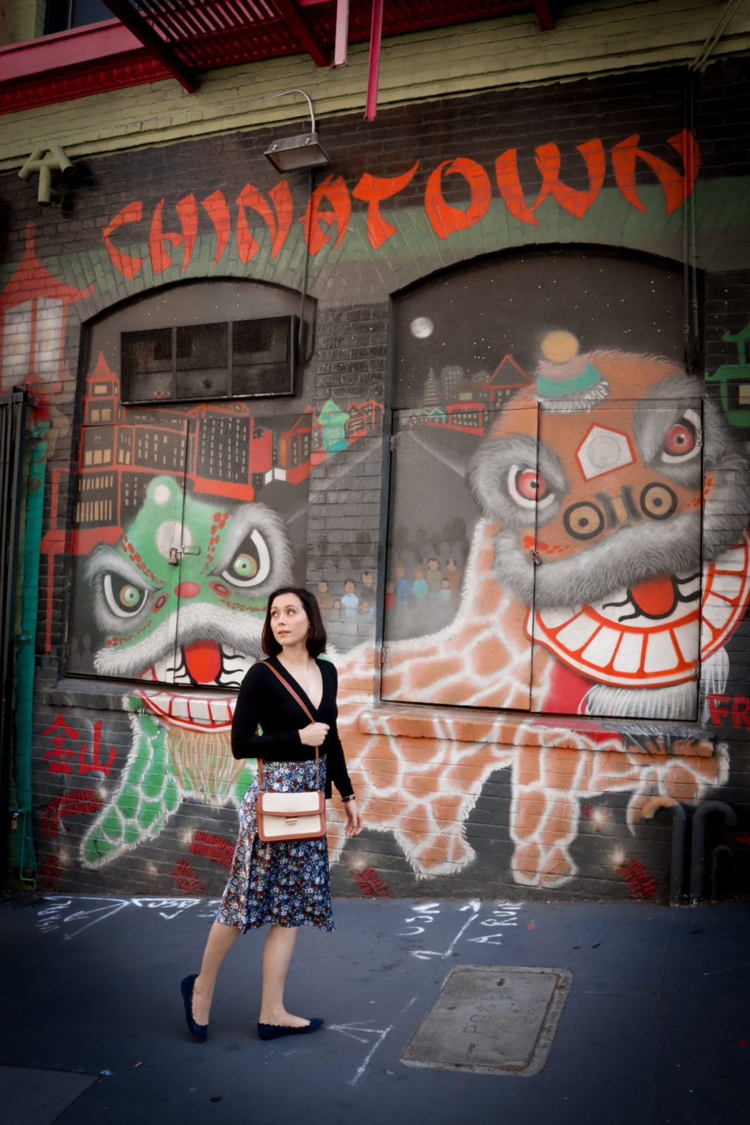 Travel Blogger Jordan Gassner looking back while walking in front of a Chinatown mural with pagodas and dragons in San Francisco