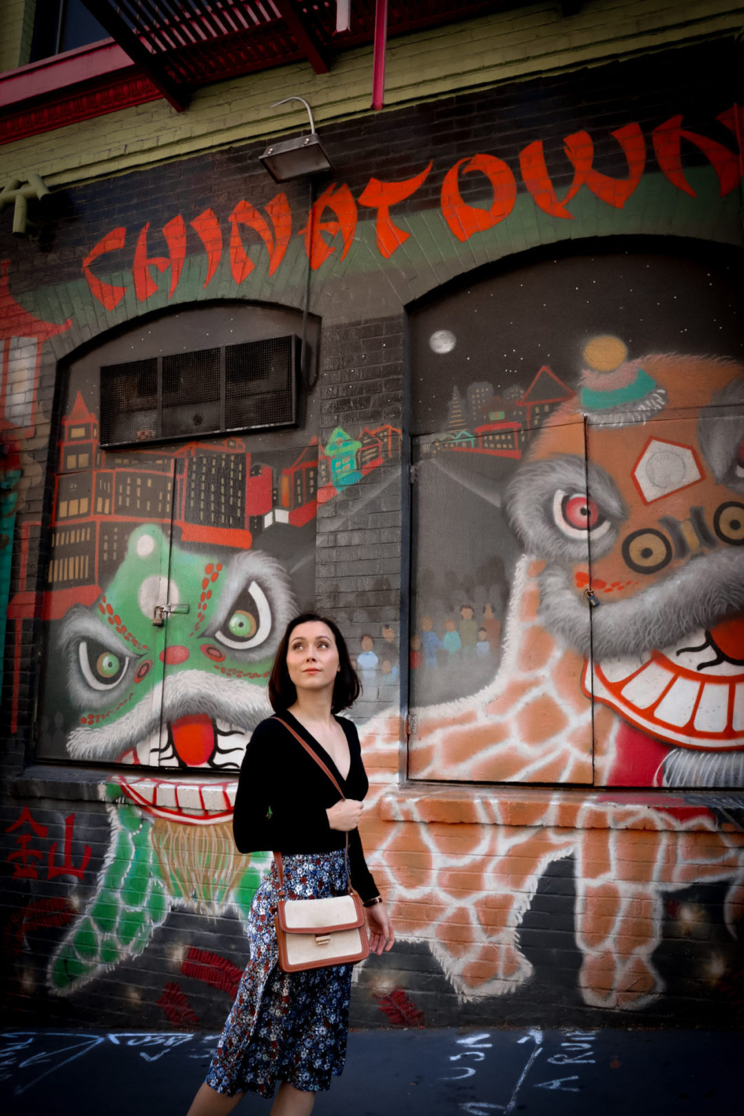 Travel Blogger Jordan Gassner standing near a Chinatown-themed mural with pagodas and dragons in San Francisco