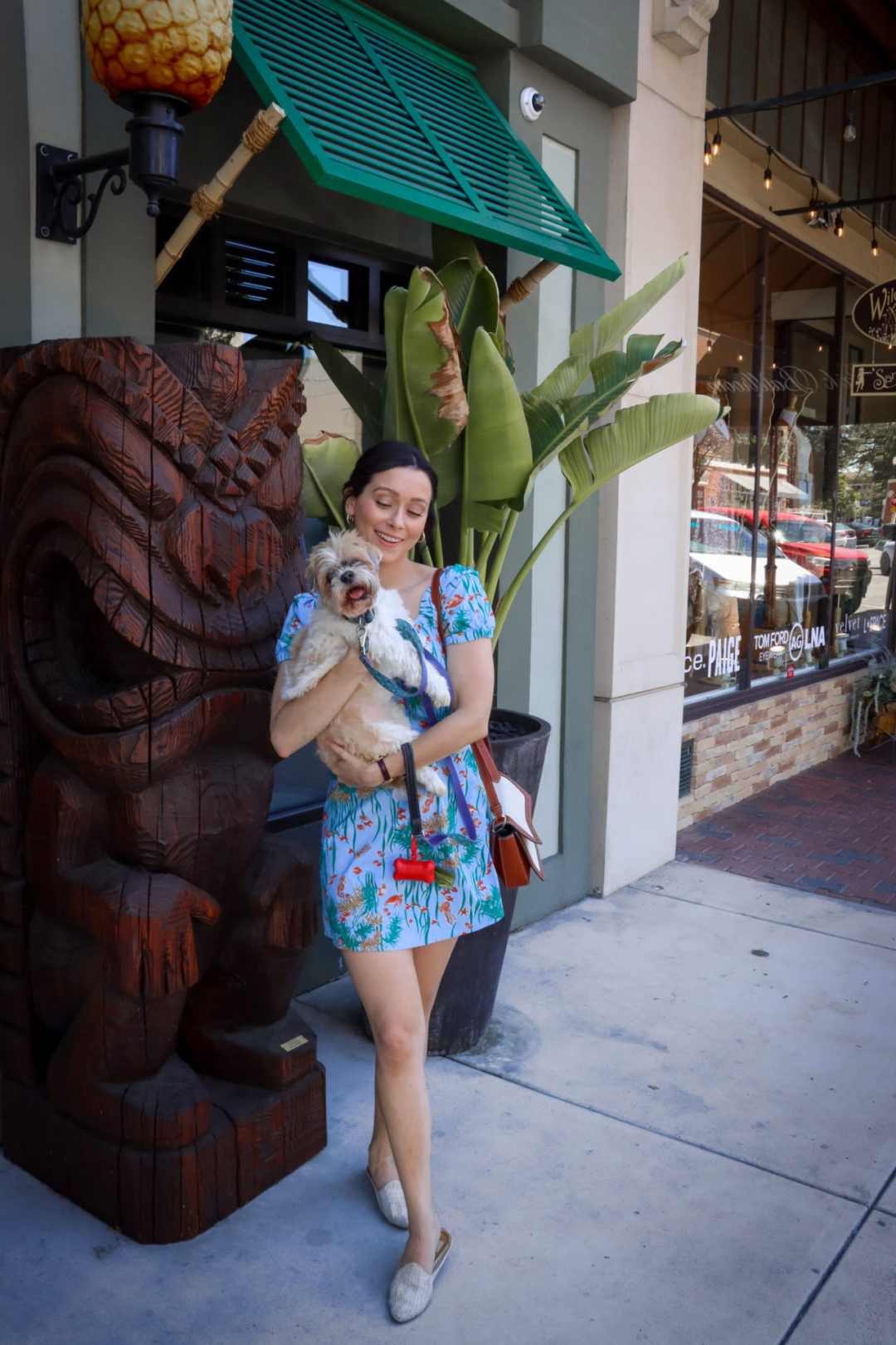 Travel Blogger Jordan Gassner smiling and holding her smiling dog, Charlie, in front of CANE TiKi Room in Paso Robles, California