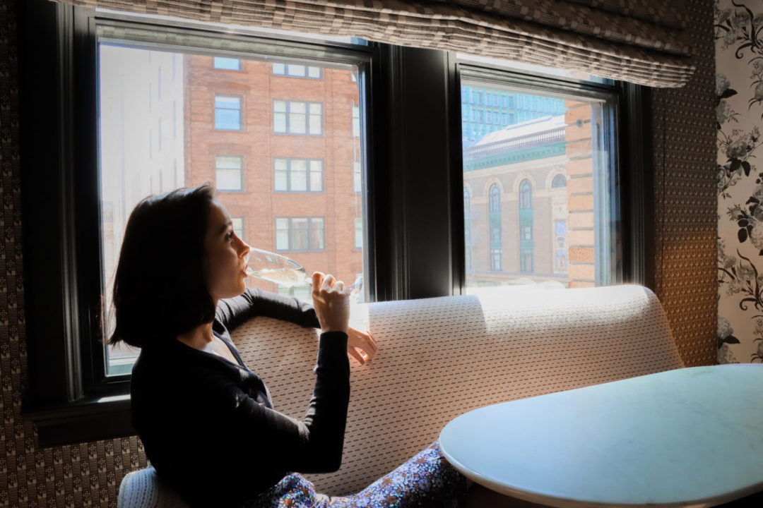Travel Blogger Jordan Gassner drinking champagne while sitting on a sofa near a window in a room at the San Francisco Proper Hotel