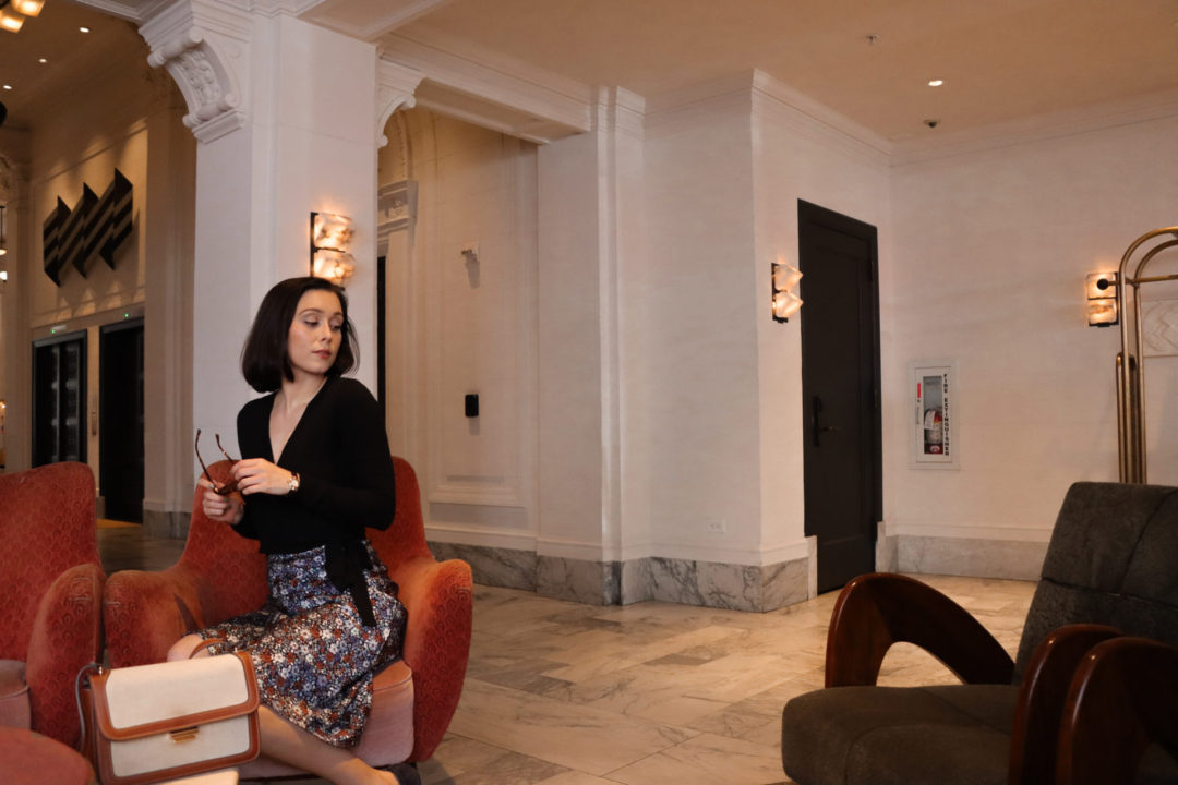 Travel Blogger Jordan Gassner sitting on a burnt orange accent chair inside the Kelly Wearstler designed San Francisco Proper Hotel Lobby