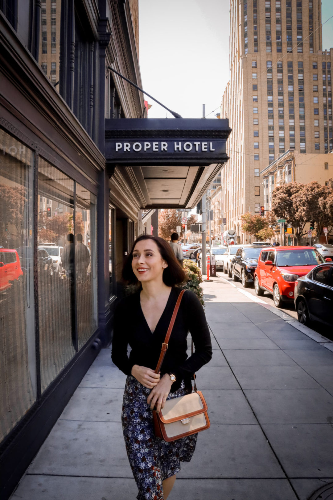 Travel Blogger Jordan Gassner smiling and holding her purse on the sidewalk in front of the front of The San Francisco Proper Hotel