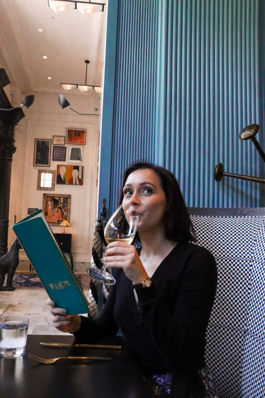 Travel Blogger Jordan Gassner drinking a glass of white wine while reading the menu inside the blue-designed restaurant, Villon in San Francisco