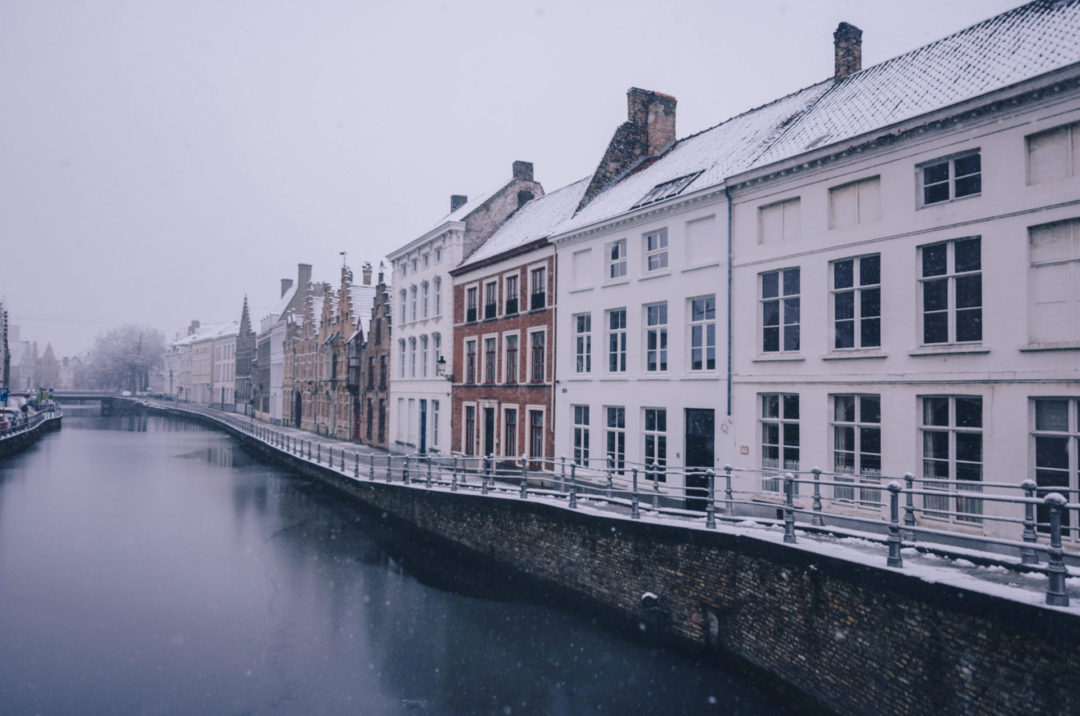 A canal in Bruges, Belgium with traditional romantic houses and shops on the right side under a layer of snow