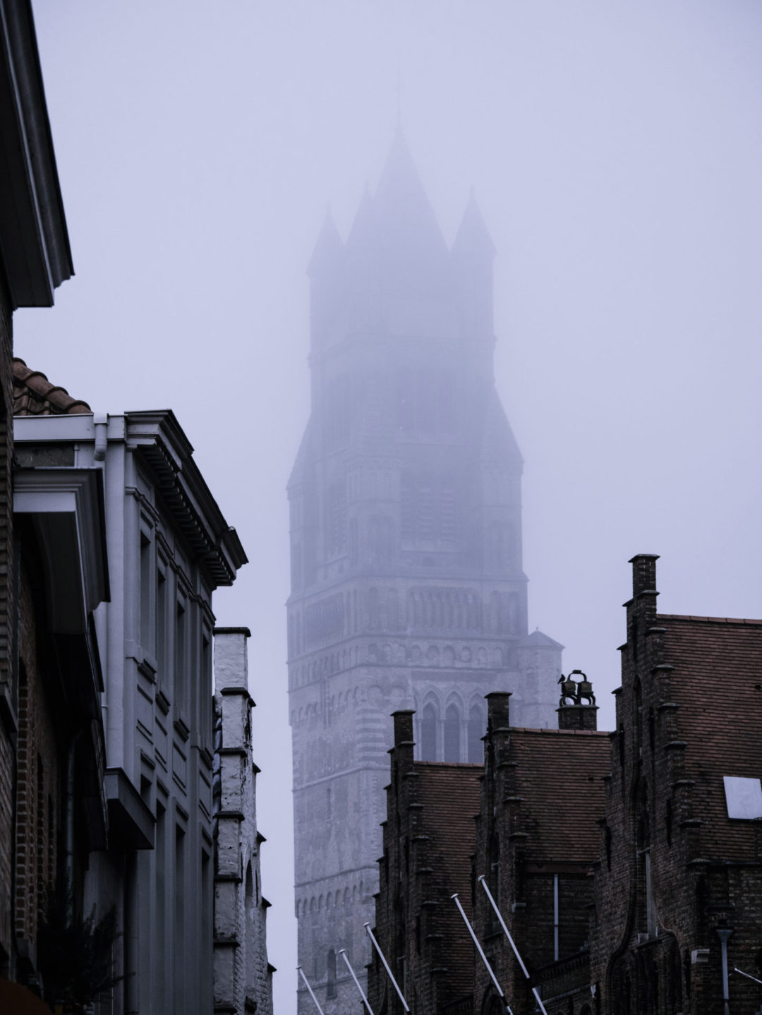 The Belfry of Bruges peeking out behind a layer of fog in winter