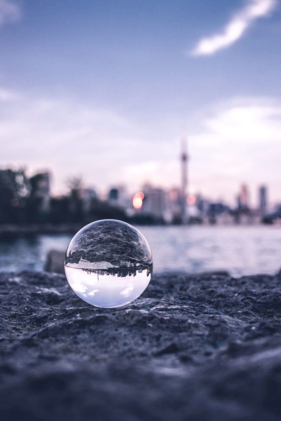 A crystal orb on a rock in front of a lake reflecting an upside-down view of the Vancouver skyline