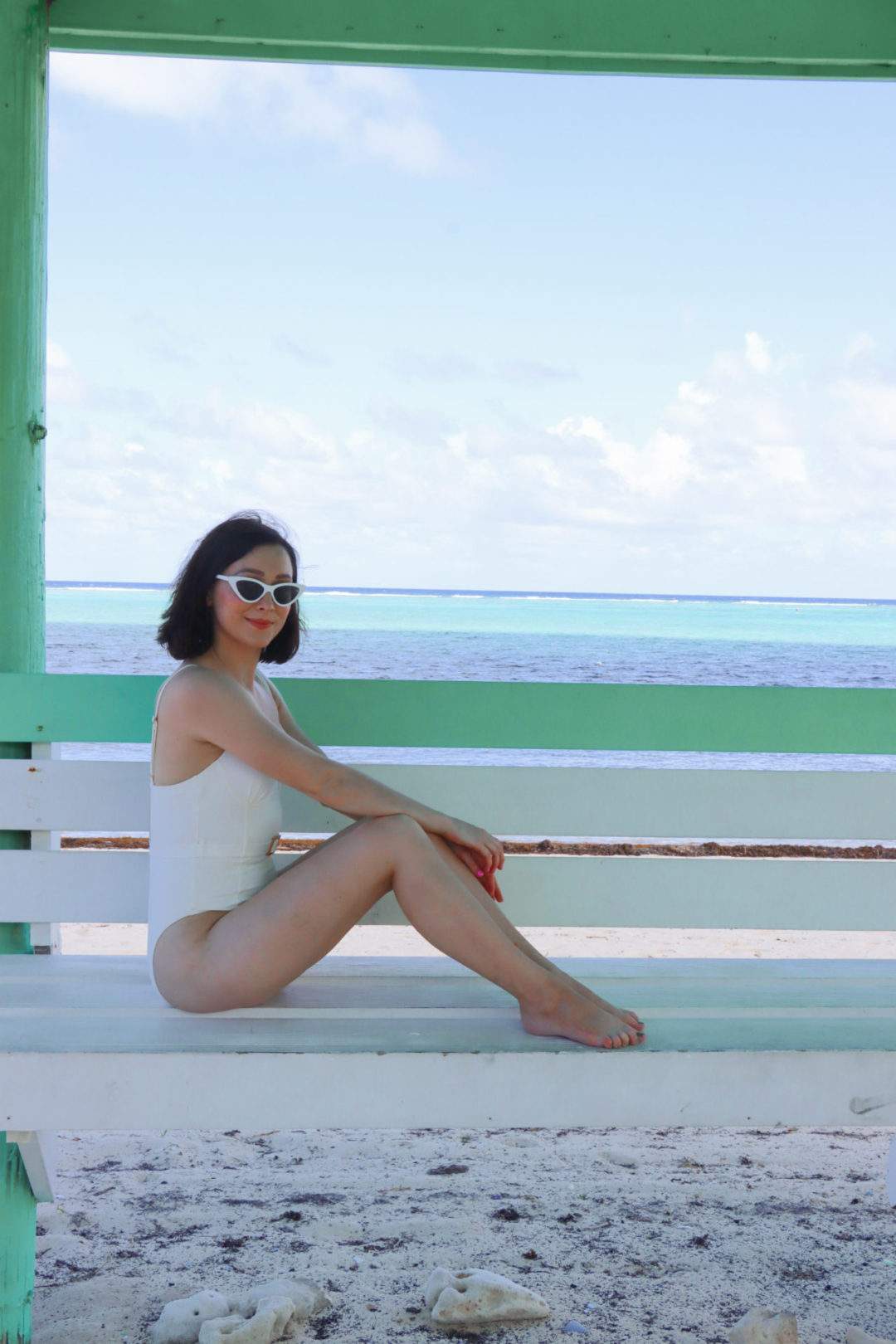 Travel Blogger Jordan Gassner sitting with legs bent under a turquoise and white beach pergola on Colliers Beach on Grand Cayman Island