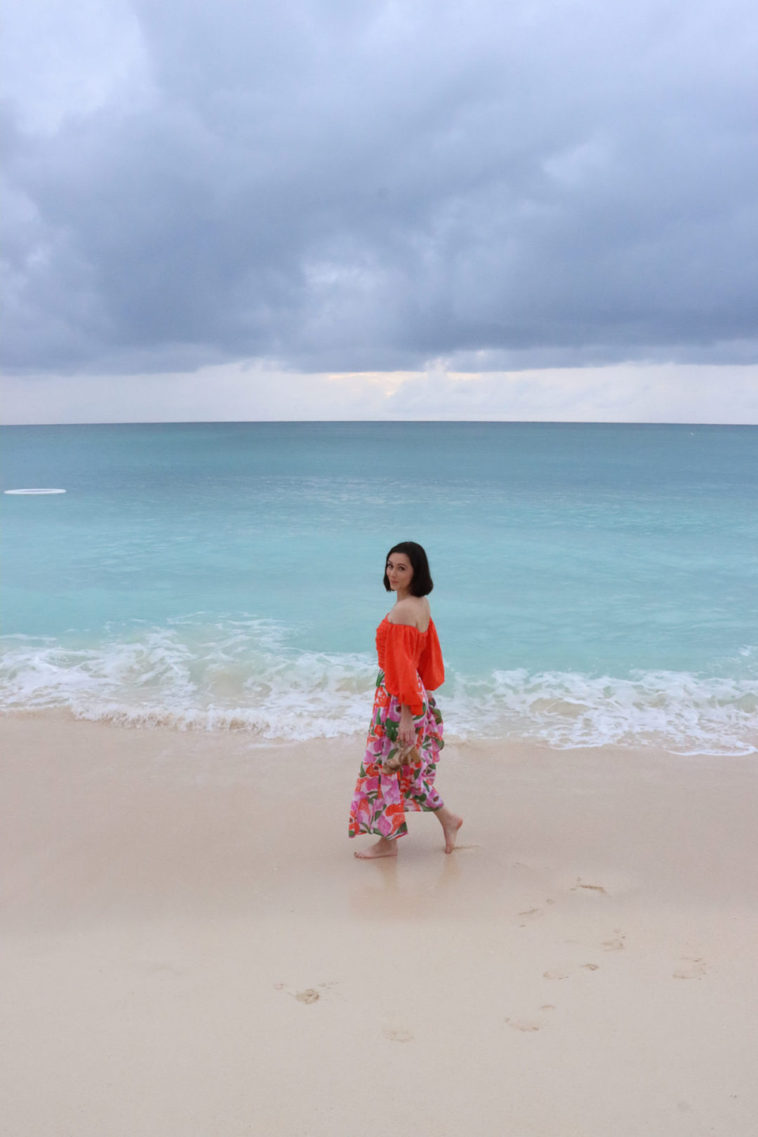 Travel Blogger Jordan Gassner smiling and looking over her shoulder while walking along Seven Mile Beach on Grand Cayman Island