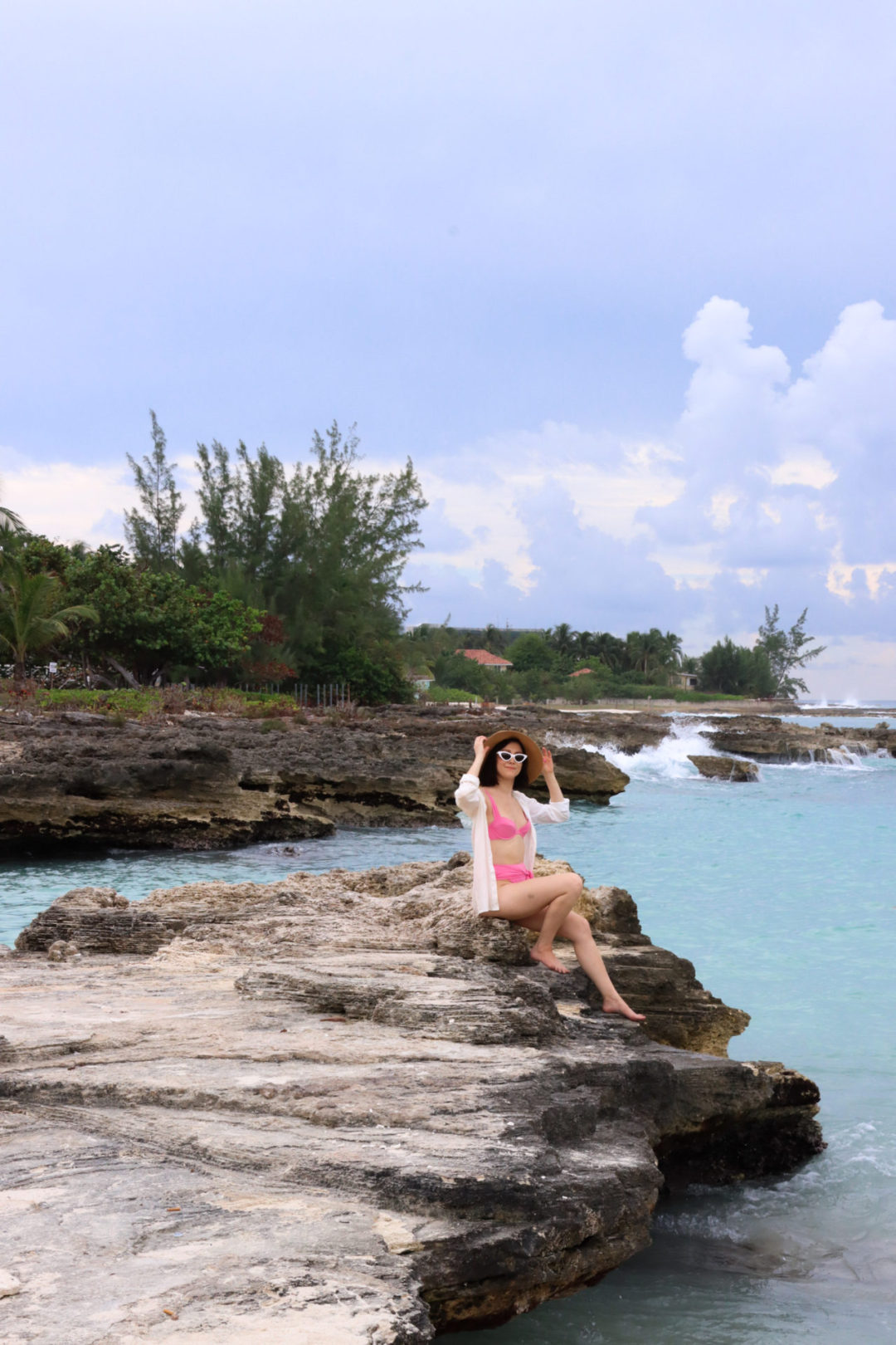 Travel Blogger Jordan Gassner sitting on an outcrop of rocks overlooking turquoise blue waters at Smith Barcadere in Grand Cayman in the Caribbean