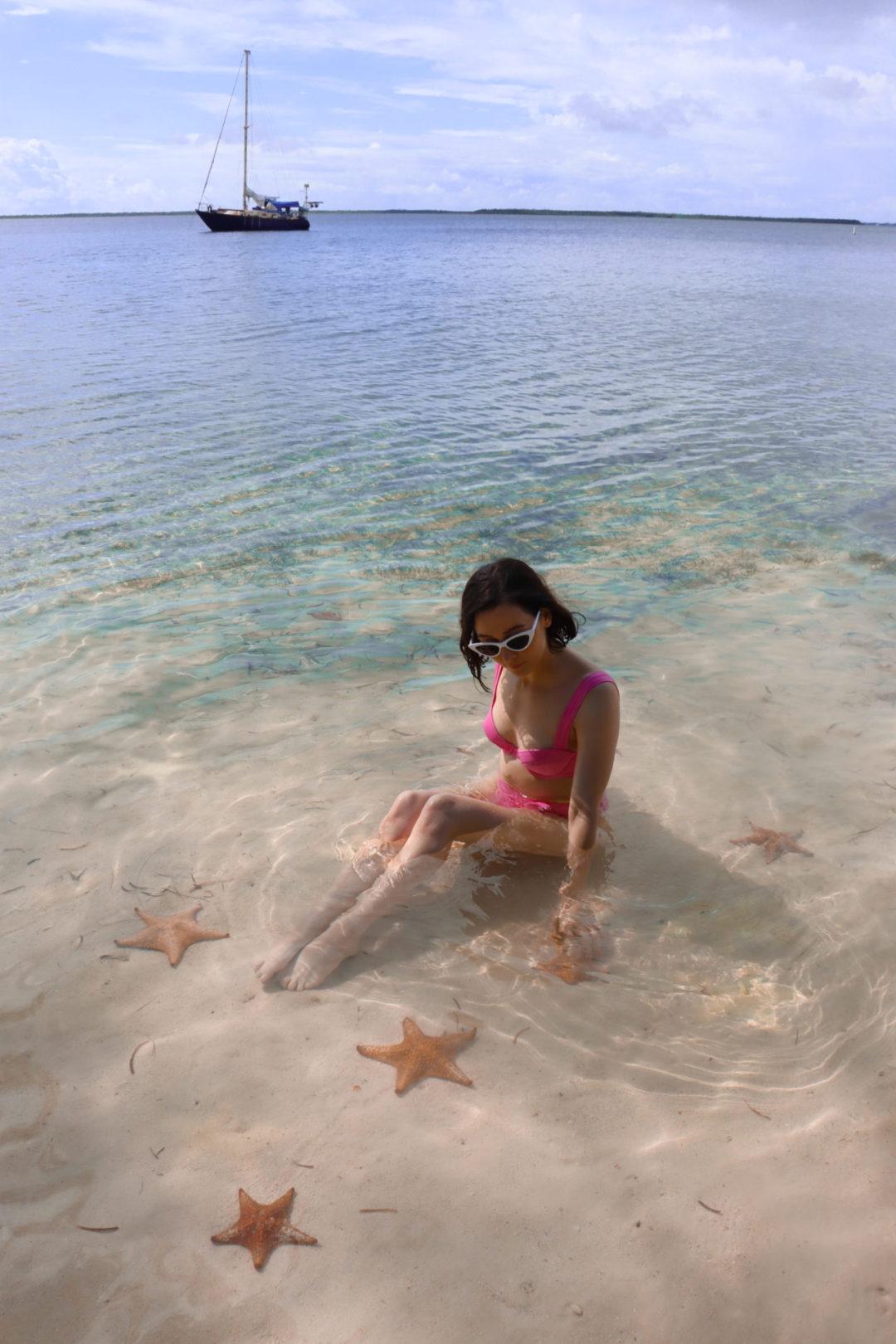 Travel Blogger Jordan Gassner sitting and reaching toward an underwater starfish at Starfish Point in the Cayman Islands