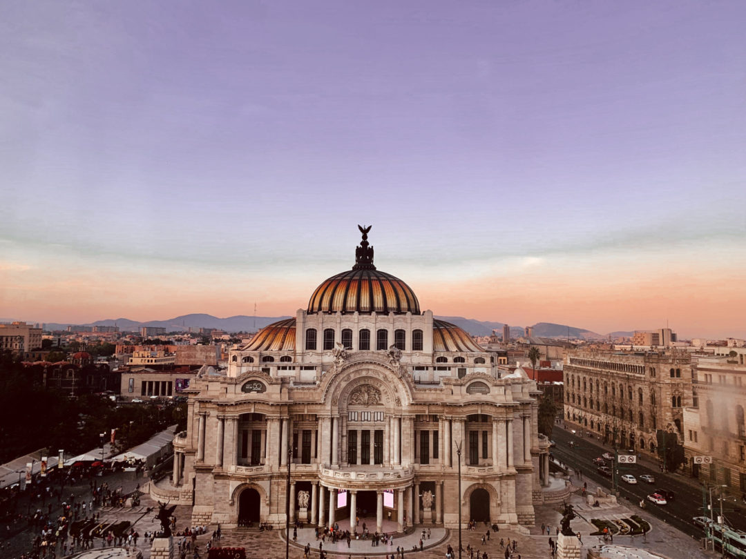 A orange and purple sunset behind the Palacio de Bellas Artes in Mexico City's El Centro neighborhood